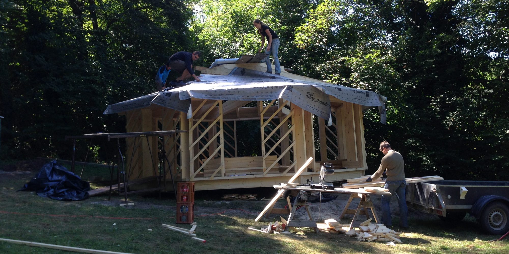 Helfer bauen das Holzgerüst der achteckigen Hütte mit Dachfolie im Wald