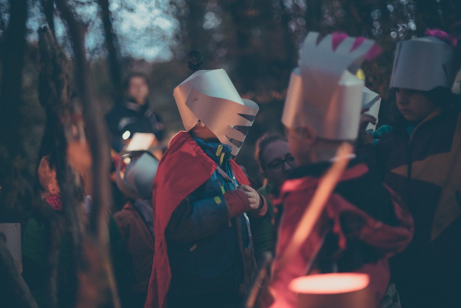 Kinder mit gebastelten Papierhelmen und Umhängen beim Laternenfest im Wald