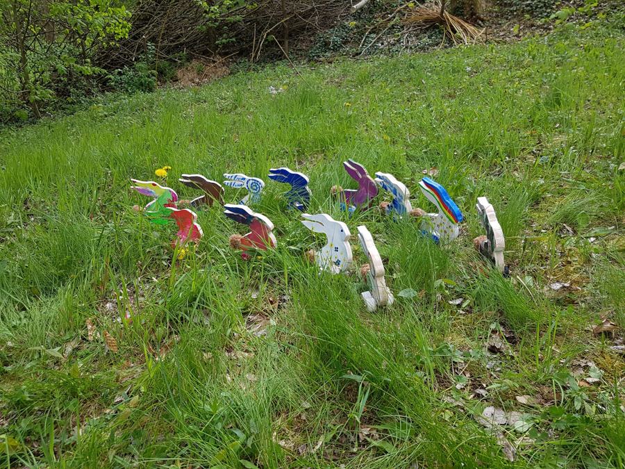 Bunt bemalte Holzhasen stehen in einer Reihe auf der Wiese