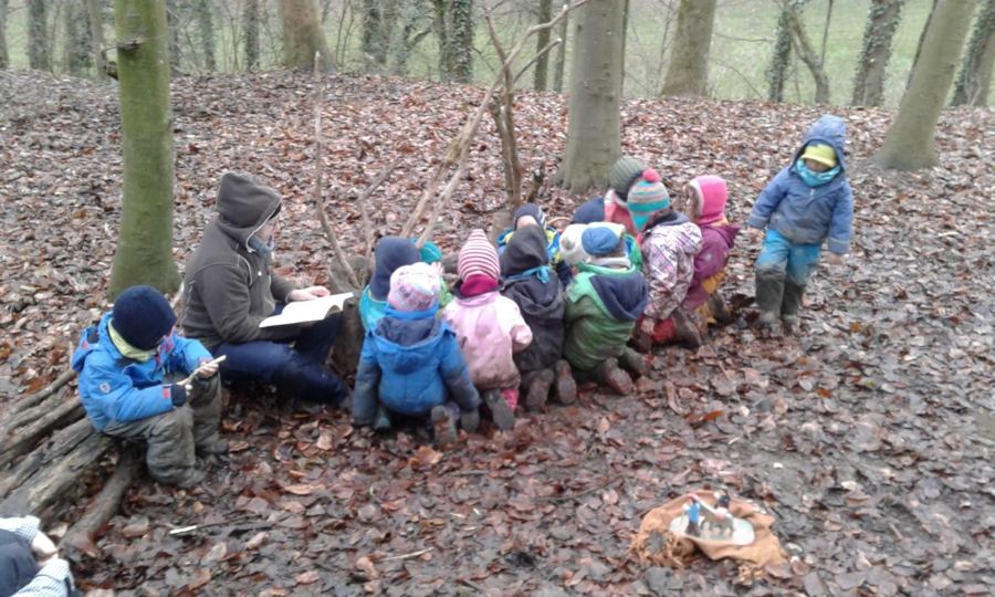 Kindergruppe sitzt im Laub, ein Erwachsener liest aus einem Buch vor
